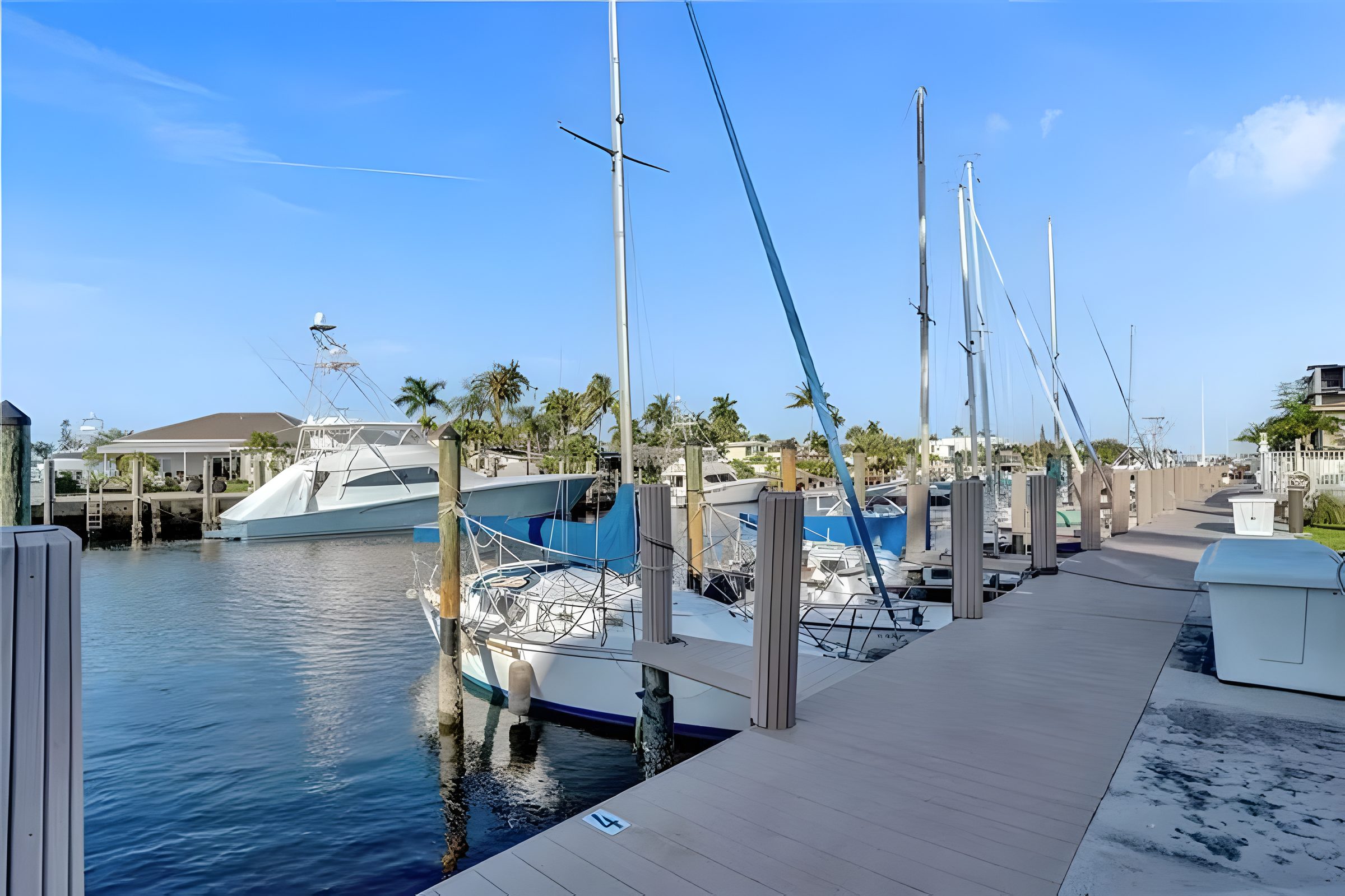 A yacht moored alongside the dock, with palms and low houses across the canal.