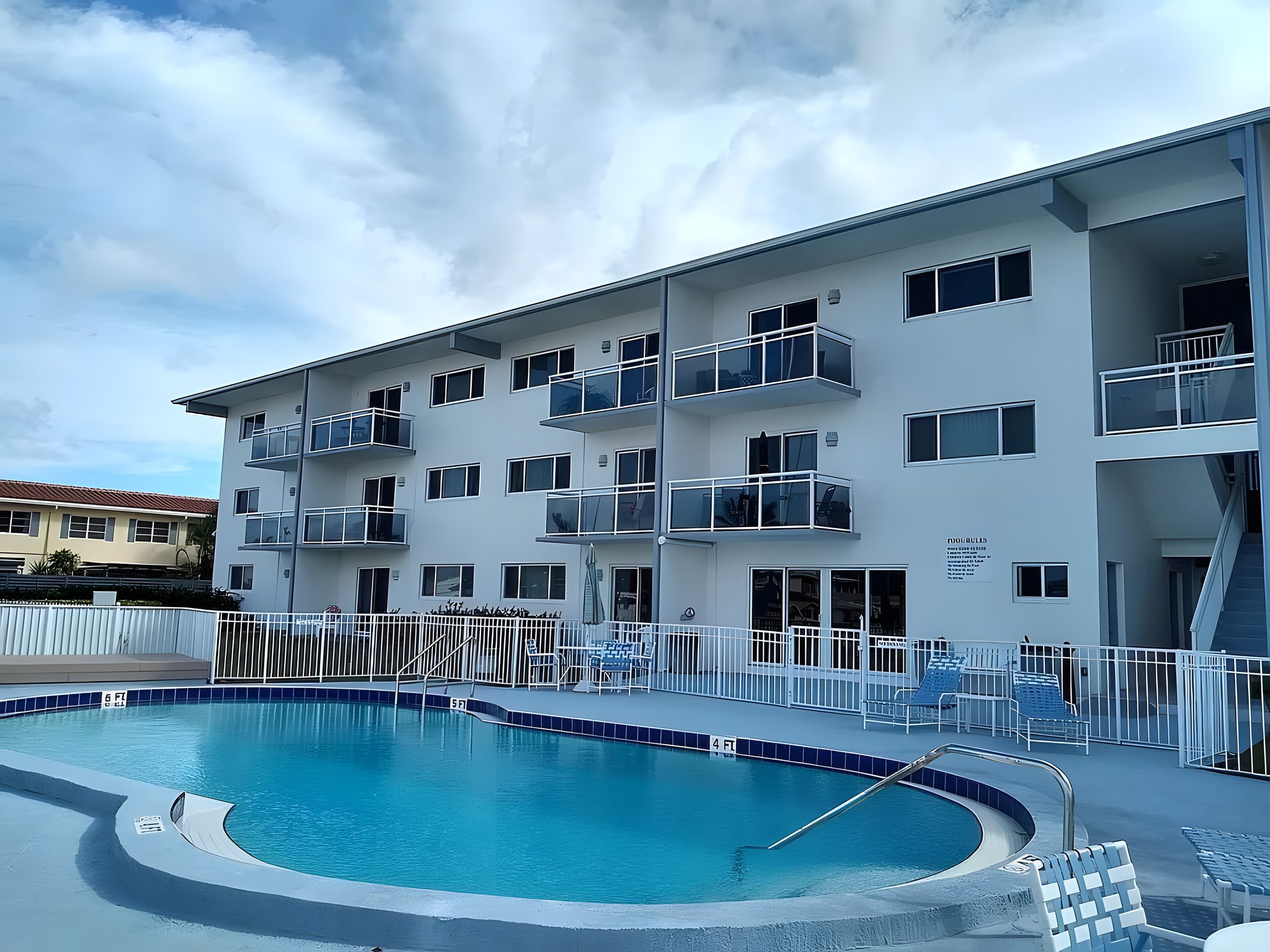 The three-storey facade of Embassy Condominiums seen across the pool, with white stucco and cantilevered balconies.